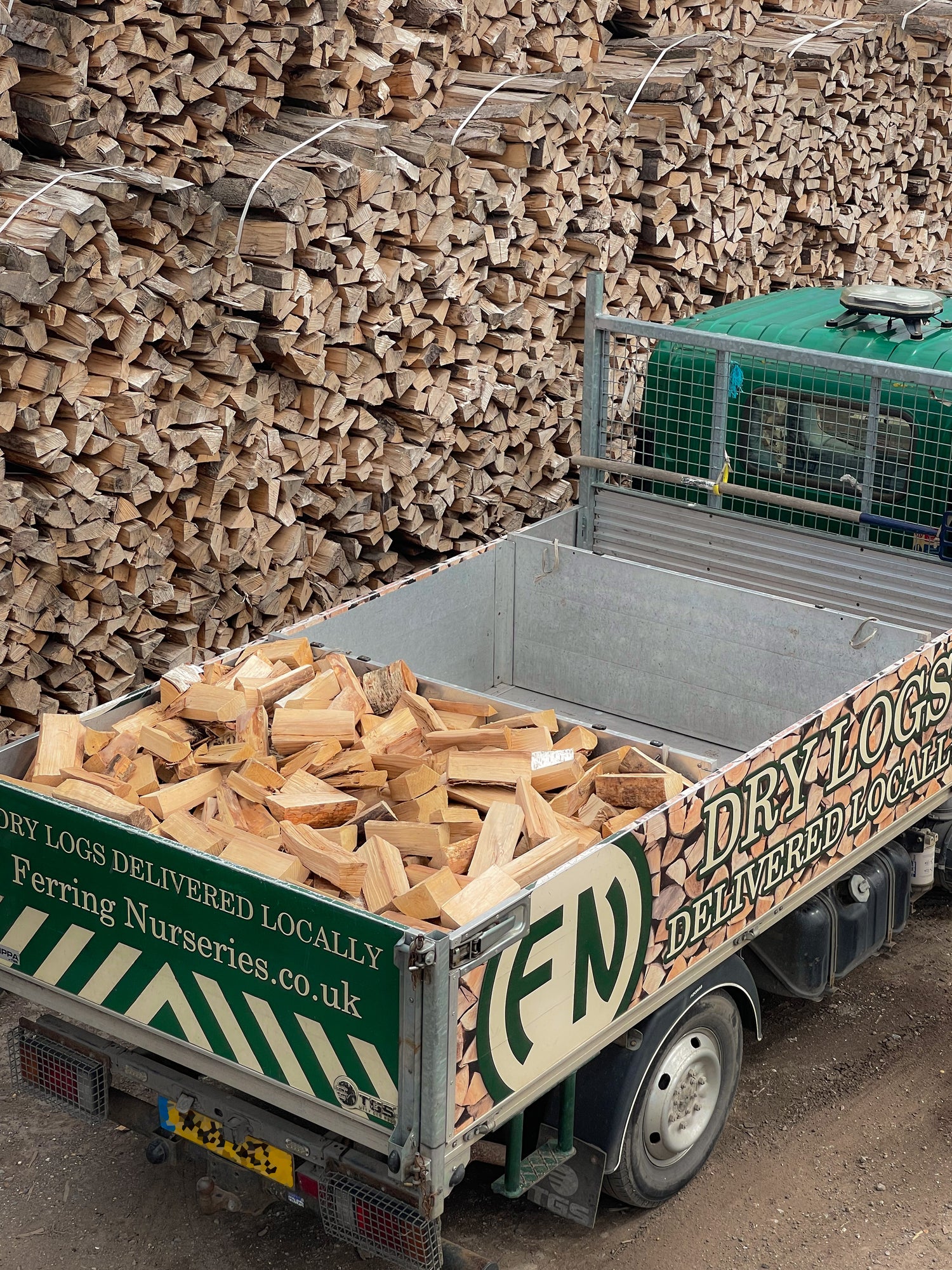 A photograph of a half load of seasoned firewood in the back of our local delivery van. Parked in front of our wood that is currently drying.