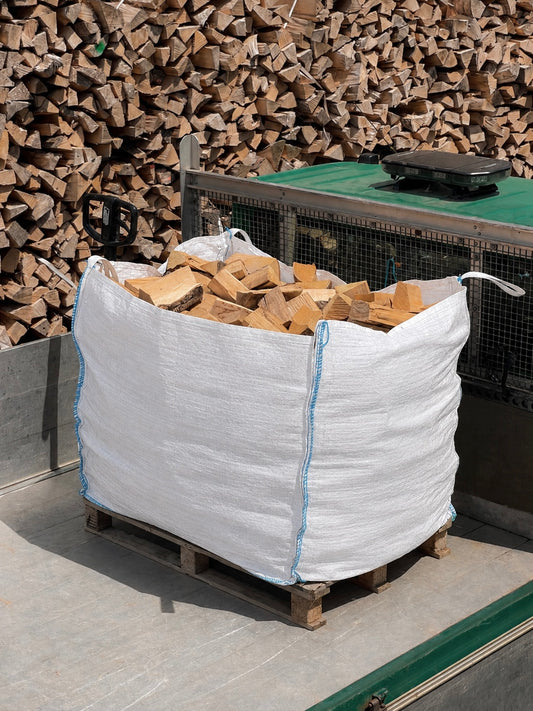 Ferring Firewood bulk bag loaded on a pallet, ready for delivery, with stacked seasoned logs in the yard behind.