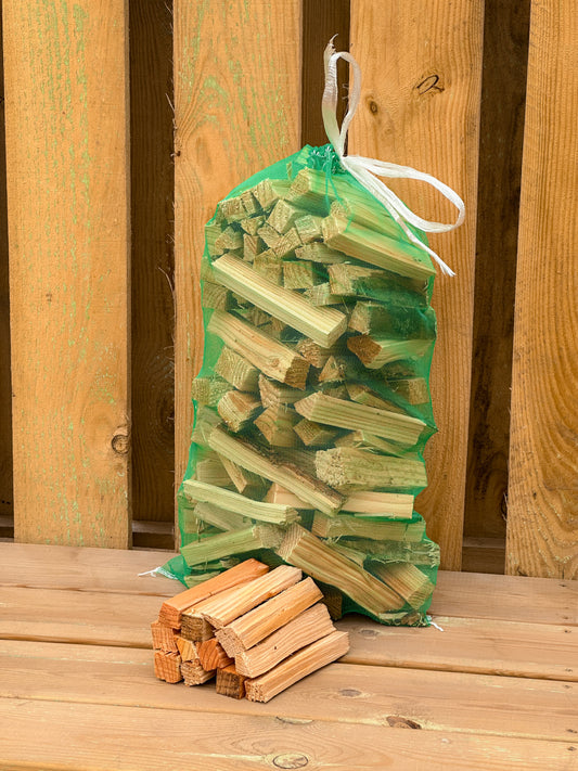 Here is a photo of our dry bags of kindling white pairs perfectly with our seasoned and kiln dried firewood. Green bag against wooden background.