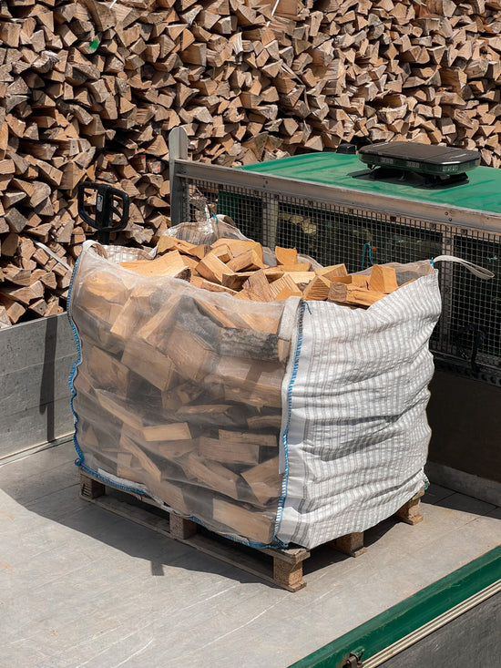 Bulk bag of seasoned firewood on the back of our local delivery van, in front of log stacks.